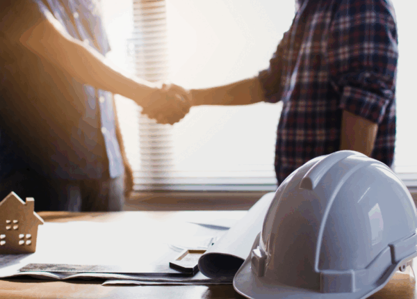 Contractor shaking hands over construction plans with a hard hat on the table, symbolizing agreement and contract in Colorado construction.